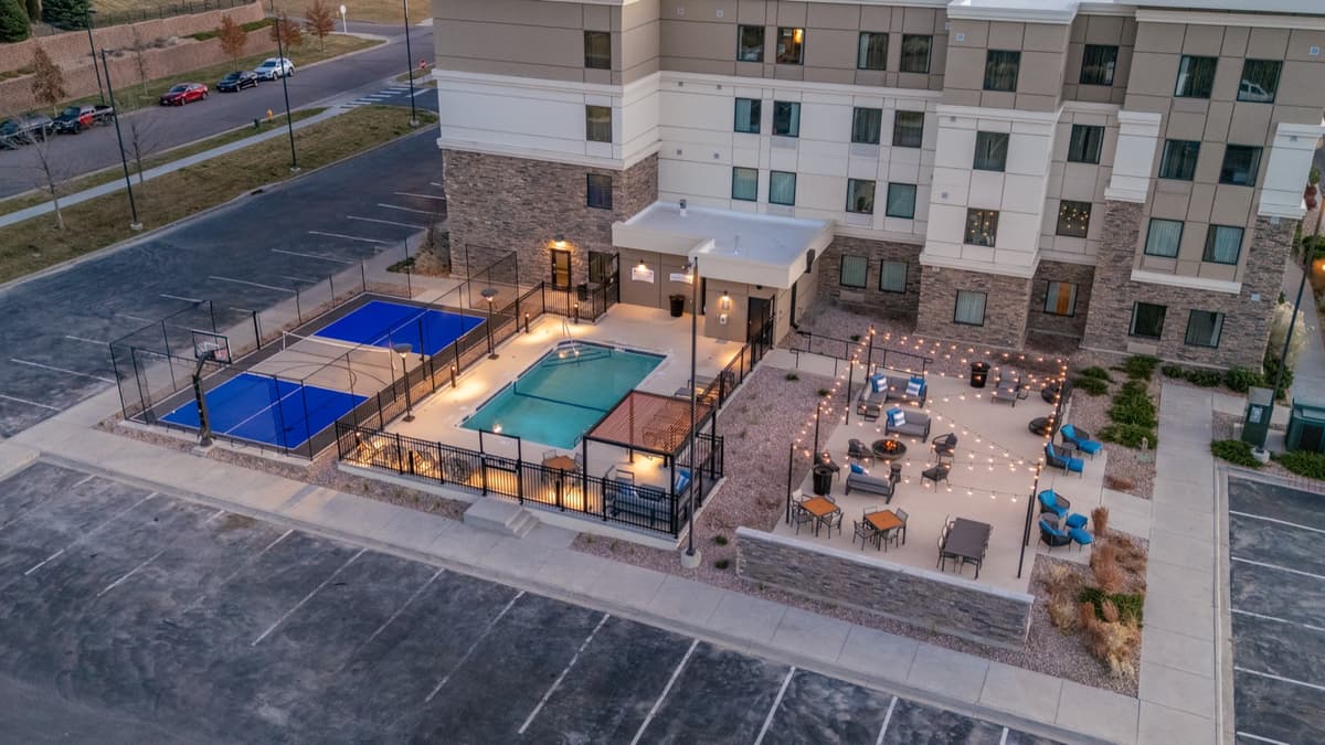 Evening aerial of the pool, pickleball court, and fire-pit patio with string lighting