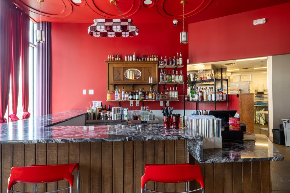 Custom bar with stone countertop, red bar stools, and vintage back bar at Velvet Lasso in Denver